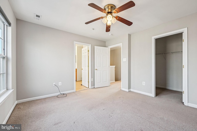 unfurnished bedroom featuring connected bathroom, a spacious closet, light colored carpet, ceiling fan, and a closet