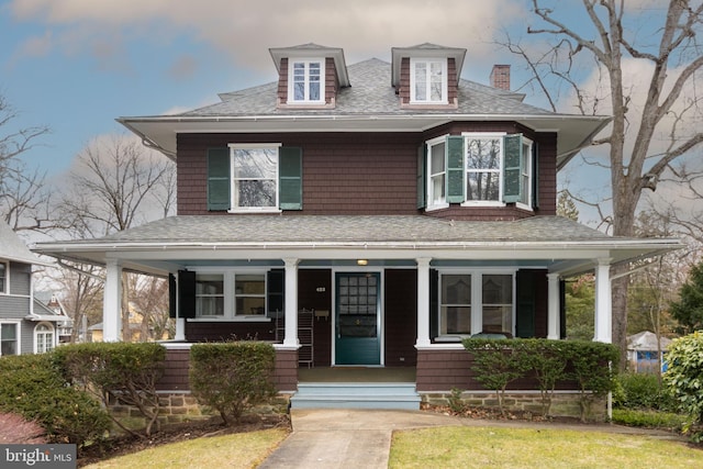 american foursquare style home with a porch, a shingled roof, and a chimney