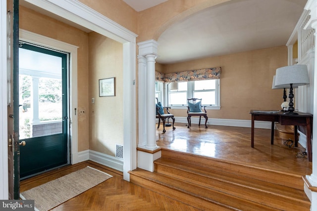 foyer featuring arched walkways, visible vents, decorative columns, and baseboards