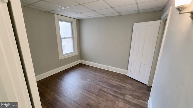 spare room with a drop ceiling and dark wood-type flooring