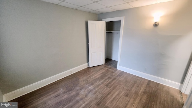 unfurnished bedroom with a drop ceiling, hardwood / wood-style flooring, and a closet