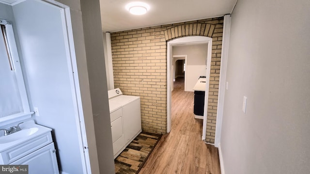 laundry area featuring brick wall, light hardwood / wood-style floors, sink, and washer and dryer