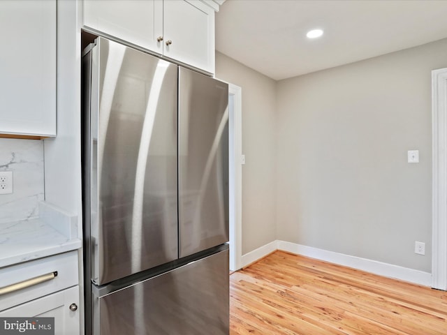 kitchen featuring stainless steel fridge, white cabinetry, backsplash, light stone countertops, and light wood-type flooring