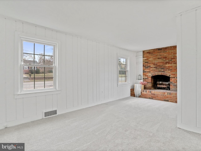 unfurnished living room with carpet floors, a brick fireplace, and a wealth of natural light