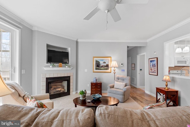 living room featuring a tile fireplace, crown molding, ceiling fan, and light wood-type flooring