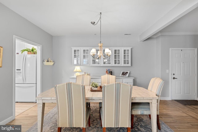 dining area with an inviting chandelier, beamed ceiling, and light wood-type flooring