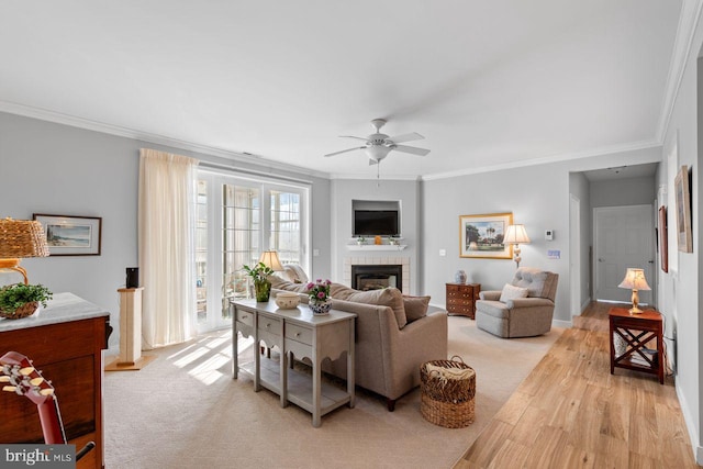 living room with crown molding, ceiling fan, a tile fireplace, and light hardwood / wood-style flooring