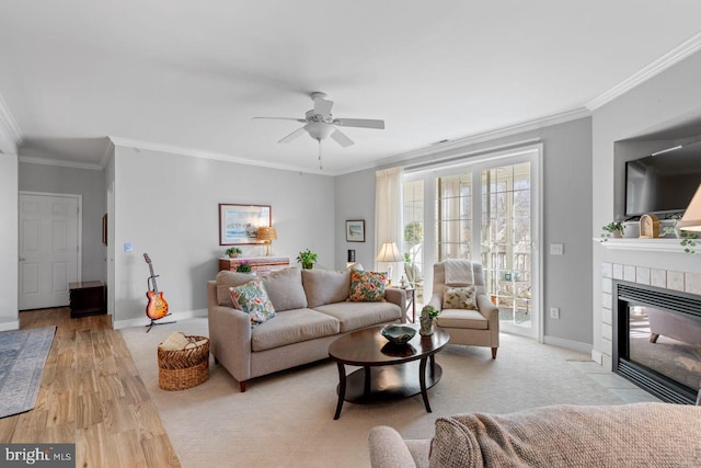 living room featuring a tiled fireplace, ornamental molding, ceiling fan, and light wood-type flooring