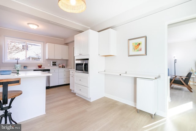 kitchen with light wood-type flooring, a breakfast bar area, white cabinets, and appliances with stainless steel finishes