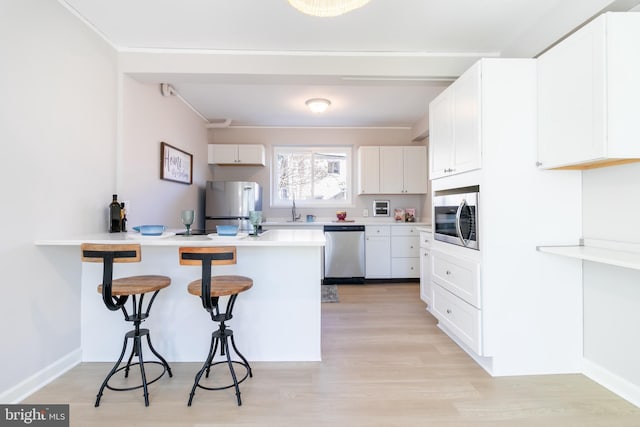 kitchen featuring appliances with stainless steel finishes, white cabinetry, a kitchen breakfast bar, kitchen peninsula, and light hardwood / wood-style flooring