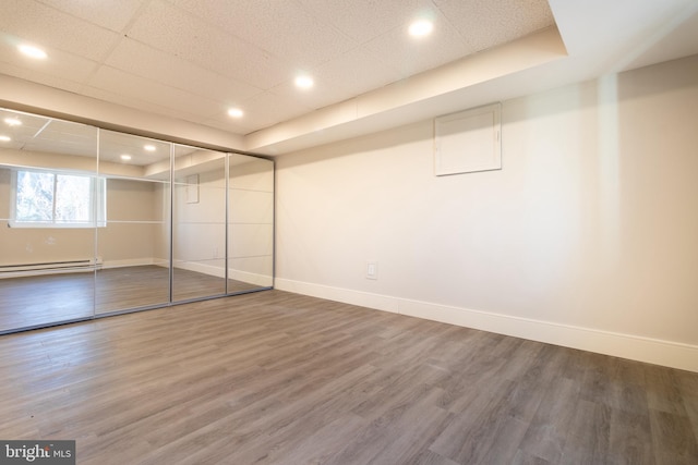 unfurnished bedroom featuring hardwood / wood-style flooring, a paneled ceiling, and a baseboard radiator