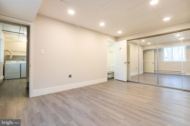 unfurnished bedroom featuring a baseboard radiator, washer and clothes dryer, light hardwood / wood-style floors, and a drop ceiling