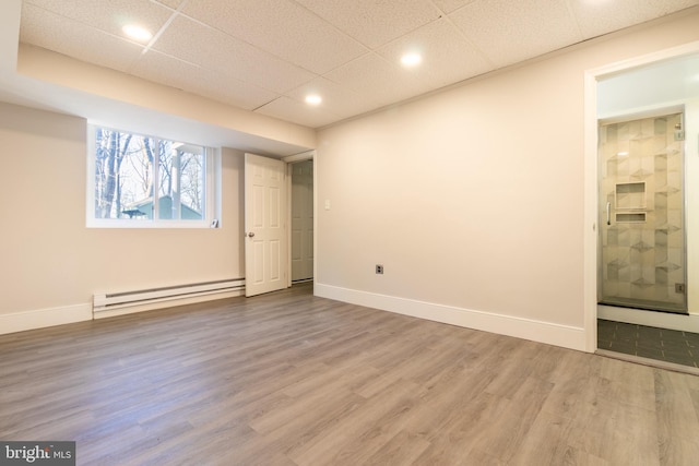 basement with a baseboard radiator, hardwood / wood-style floors, and a drop ceiling