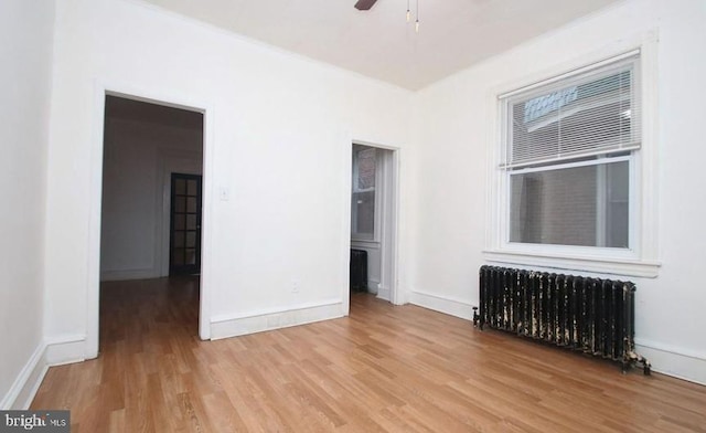 empty room featuring ceiling fan, radiator, and light hardwood / wood-style floors