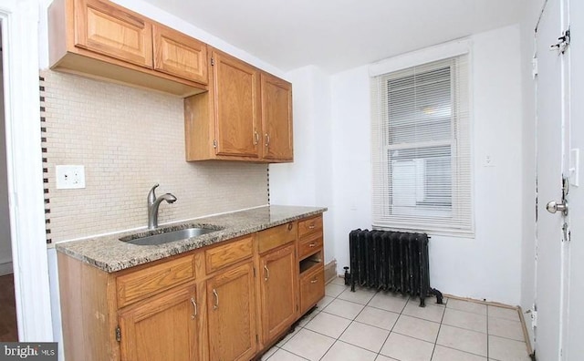 kitchen with light tile patterned flooring, radiator, sink, decorative backsplash, and light stone counters