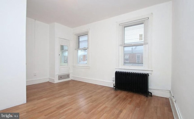 unfurnished room with a healthy amount of sunlight, radiator heating unit, and light wood-type flooring