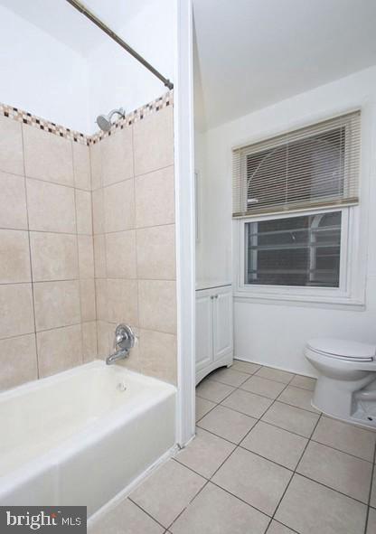 bathroom with tile patterned flooring, tiled shower / bath combo, and toilet