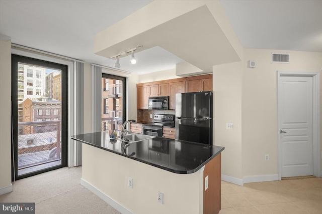 kitchen featuring sink, track lighting, black appliances, a center island with sink, and light carpet