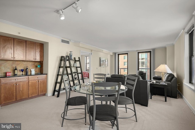 carpeted dining area with rail lighting and ornamental molding