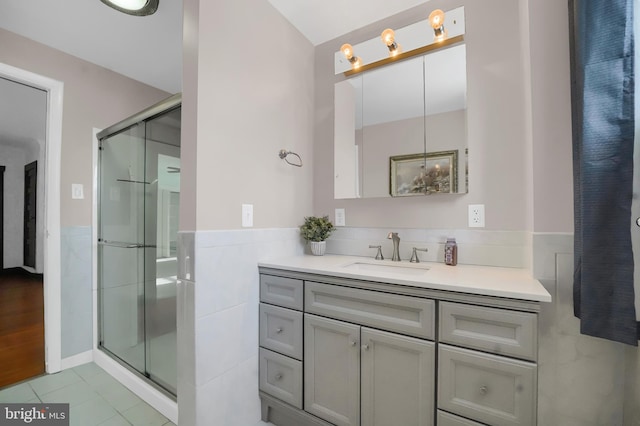 bathroom featuring vanity, tile patterned flooring, a shower with shower door, and tile walls