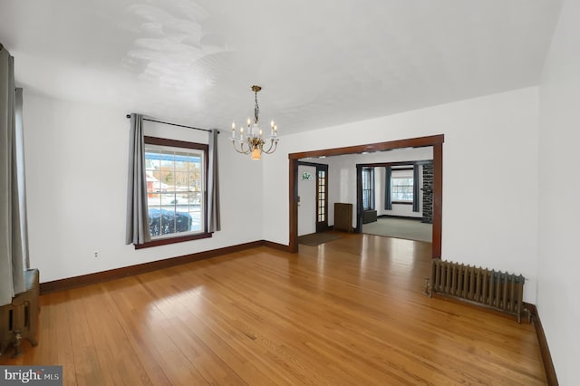 spare room with a wealth of natural light, wood-type flooring, radiator heating unit, and a notable chandelier