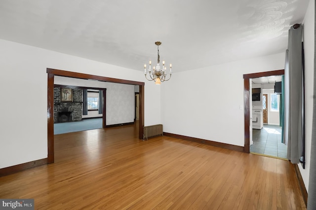 unfurnished room featuring an inviting chandelier, radiator, a fireplace, and hardwood / wood-style floors