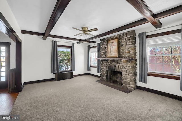 unfurnished living room featuring beamed ceiling, a stone fireplace, radiator, and carpet