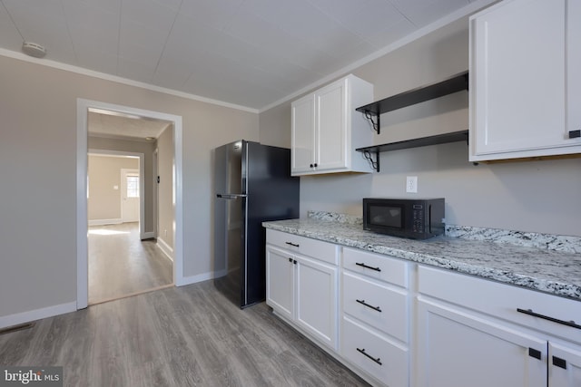 kitchen featuring white cabinetry, light stone counters, black appliances, crown molding, and light wood-type flooring