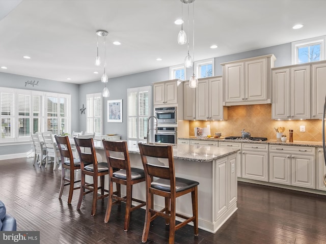 kitchen with an island with sink, dark hardwood / wood-style floors, light stone counters, and decorative light fixtures