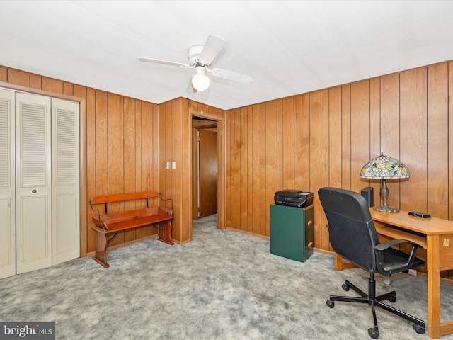 carpeted office space with a ceiling fan and wood walls