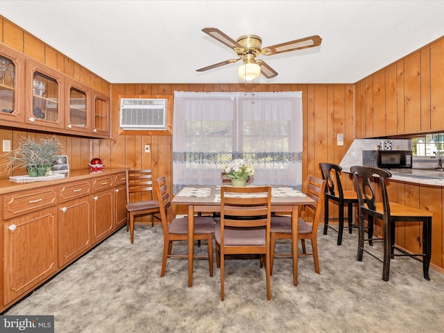 dining area featuring light carpet, an AC wall unit, wood walls, and ceiling fan