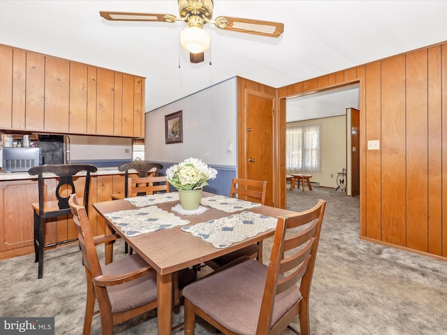 dining space featuring a ceiling fan, light carpet, and wood walls