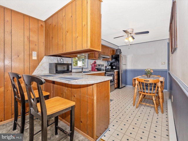 kitchen with a ceiling fan, brown cabinets, a peninsula, stainless steel appliances, and light countertops