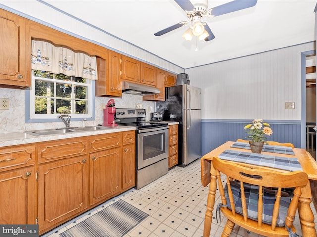 kitchen featuring a wainscoted wall, stainless steel appliances, light countertops, a sink, and under cabinet range hood