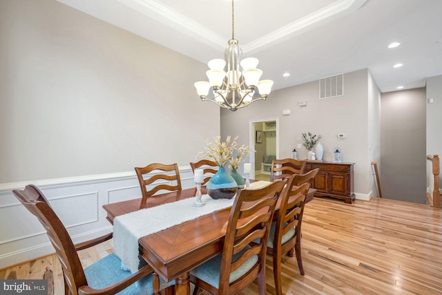 dining area with crown molding, a tray ceiling, light hardwood / wood-style flooring, and a notable chandelier