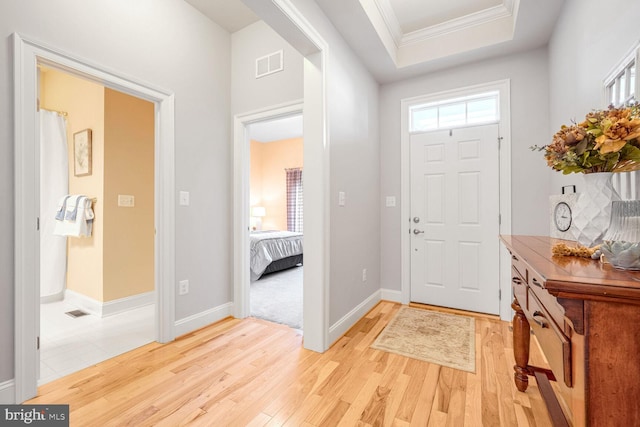 entryway with crown molding, a tray ceiling, and light wood-type flooring