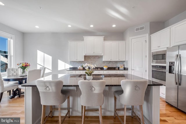 kitchen featuring white cabinetry, a breakfast bar area, stainless steel appliances, and a center island with sink