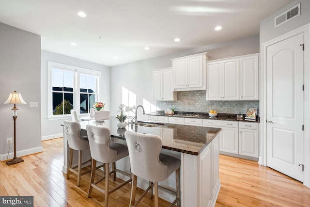 kitchen featuring sink, white cabinetry, dark stone countertops, tasteful backsplash, and light hardwood / wood-style floors