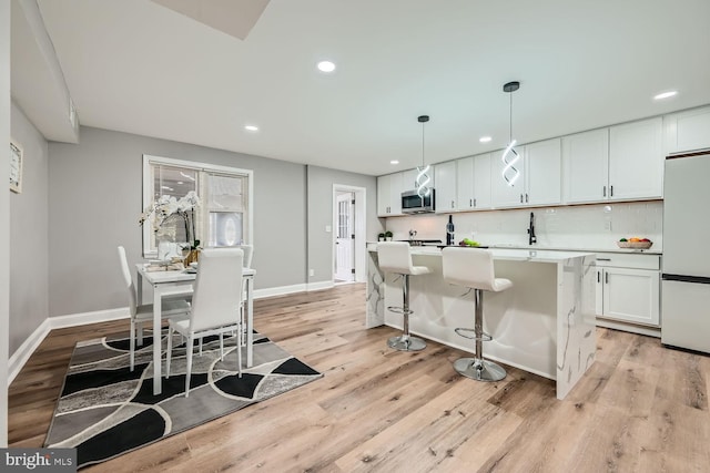 kitchen with pendant lighting, white cabinets, white fridge, a center island, and light hardwood / wood-style floors