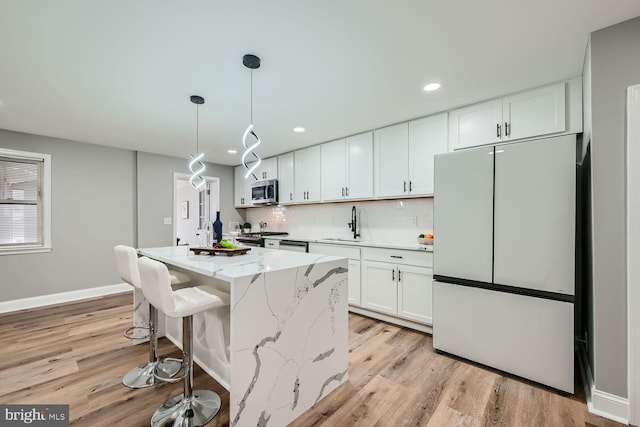 kitchen with stainless steel appliances, hanging light fixtures, white cabinets, and light stone counters