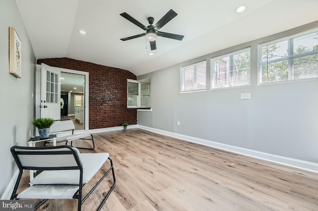 sitting room with ceiling fan, brick wall, lofted ceiling, and light wood-type flooring