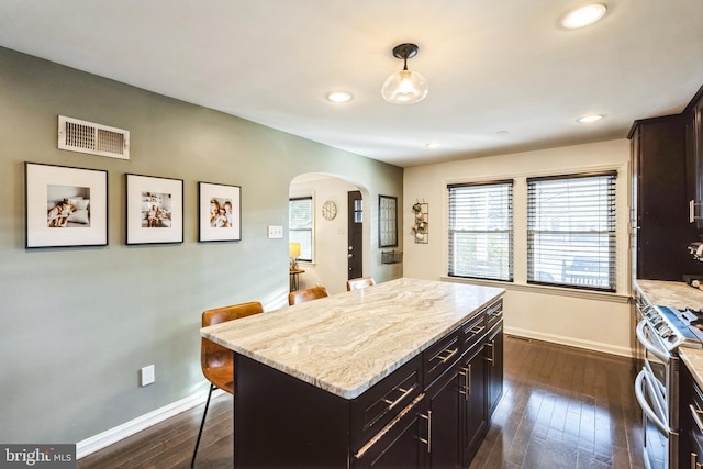 kitchen featuring stainless steel stove, a kitchen breakfast bar, light stone countertops, a kitchen island, and decorative light fixtures