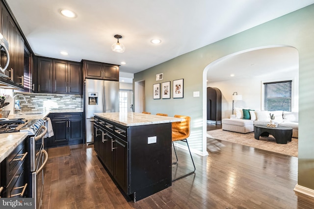 kitchen with stainless steel appliances, a center island, dark wood-type flooring, and light stone counters