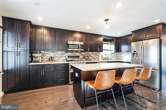 kitchen with dark brown cabinets, appliances with stainless steel finishes, wood-type flooring, and a kitchen island