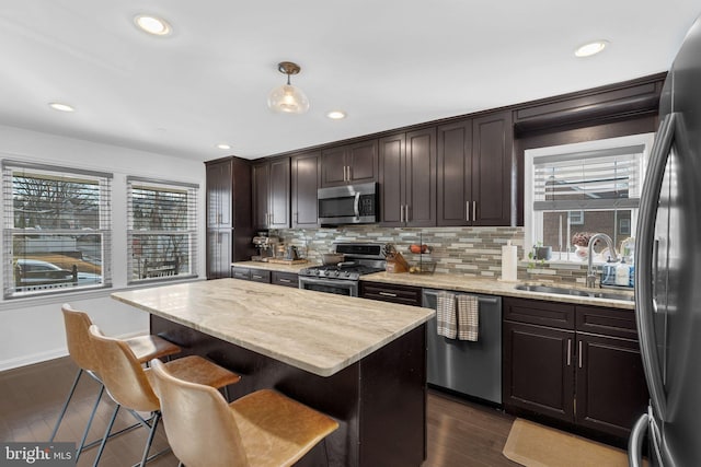 kitchen featuring sink, hanging light fixtures, stainless steel appliances, a center island, and dark brown cabinetry