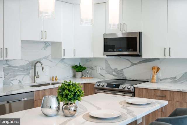 kitchen with sink, backsplash, stainless steel appliances, light stone counters, and white cabinets