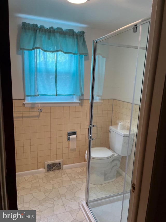 bathroom with tile walls, tile patterned flooring, a shower with shower door, and toilet