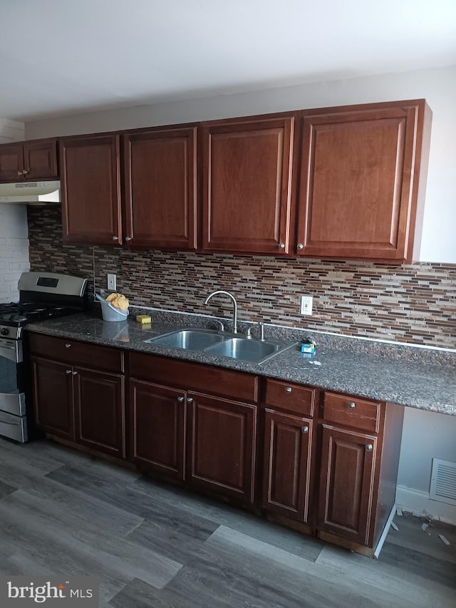 kitchen featuring dark wood-type flooring, stainless steel gas range, sink, and backsplash