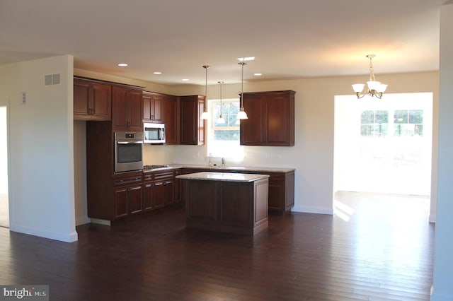 kitchen with appliances with stainless steel finishes, decorative light fixtures, dark hardwood / wood-style flooring, and a kitchen island