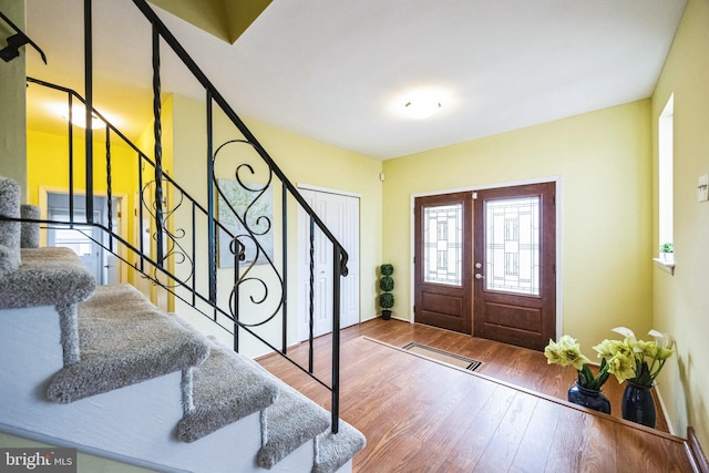 foyer with a healthy amount of sunlight, stairs, visible vents, and wood finished floors